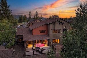 Una casa de dos pisos con un patio, un área de estar techada al aire libre y vistas del bosque circundante.