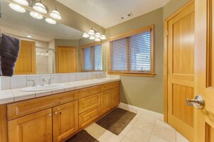 Un baño con tocador doble, armarios de madera, un espejo grande y una ventana con persianas.