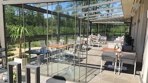An outdoor patio with glass walls, tables, chairs, and a pergola. - Solidaris (Kedzierzyn Kozle)