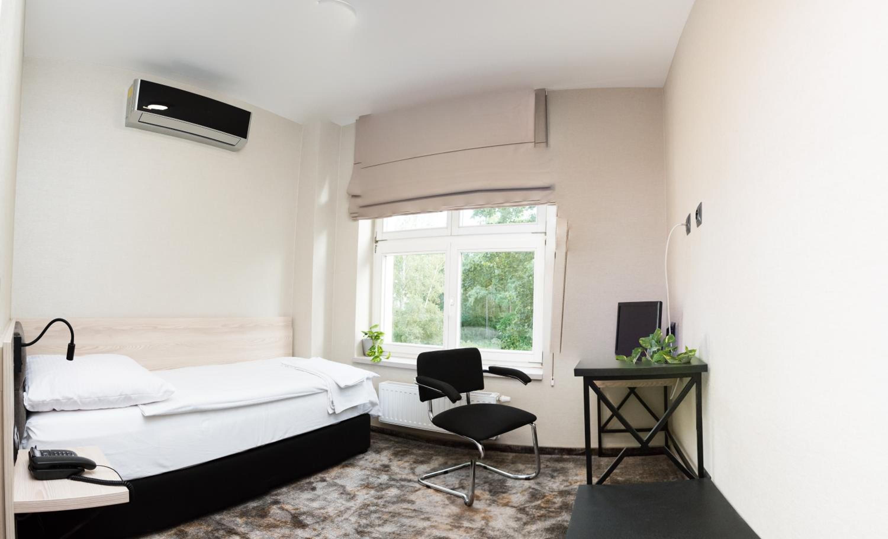 Ein Hotelzimmer mit Bett, Schreibtisch, Stuhl, Heizkörper und Fenster mit Blick ins Grüne.