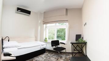 Ein Hotelzimmer mit Bett, Schreibtisch, Stuhl, Heizkörper und Fenster mit Blick ins Grüne.