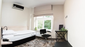 A hotel room with a bed, a desk, a chair, a radiator, and a window with a view of greenery. - Solidaris (Kedzierzyn Kozle)