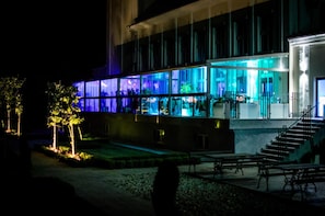 Un edificio moderno con amplios ventanales de vidrio, una escalera y mobiliario exterior.