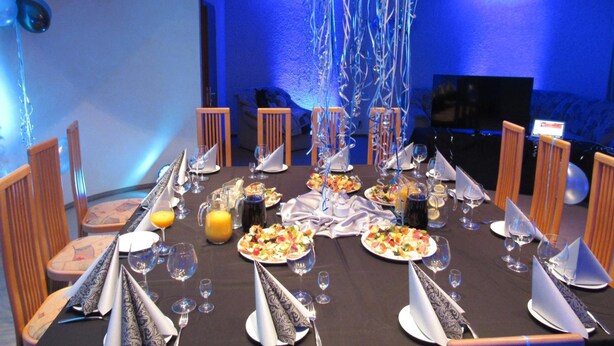 A dining area with a long table set for a meal, chairs, and a television in the background. - Solidaris (Kedzierzyn Kozle)