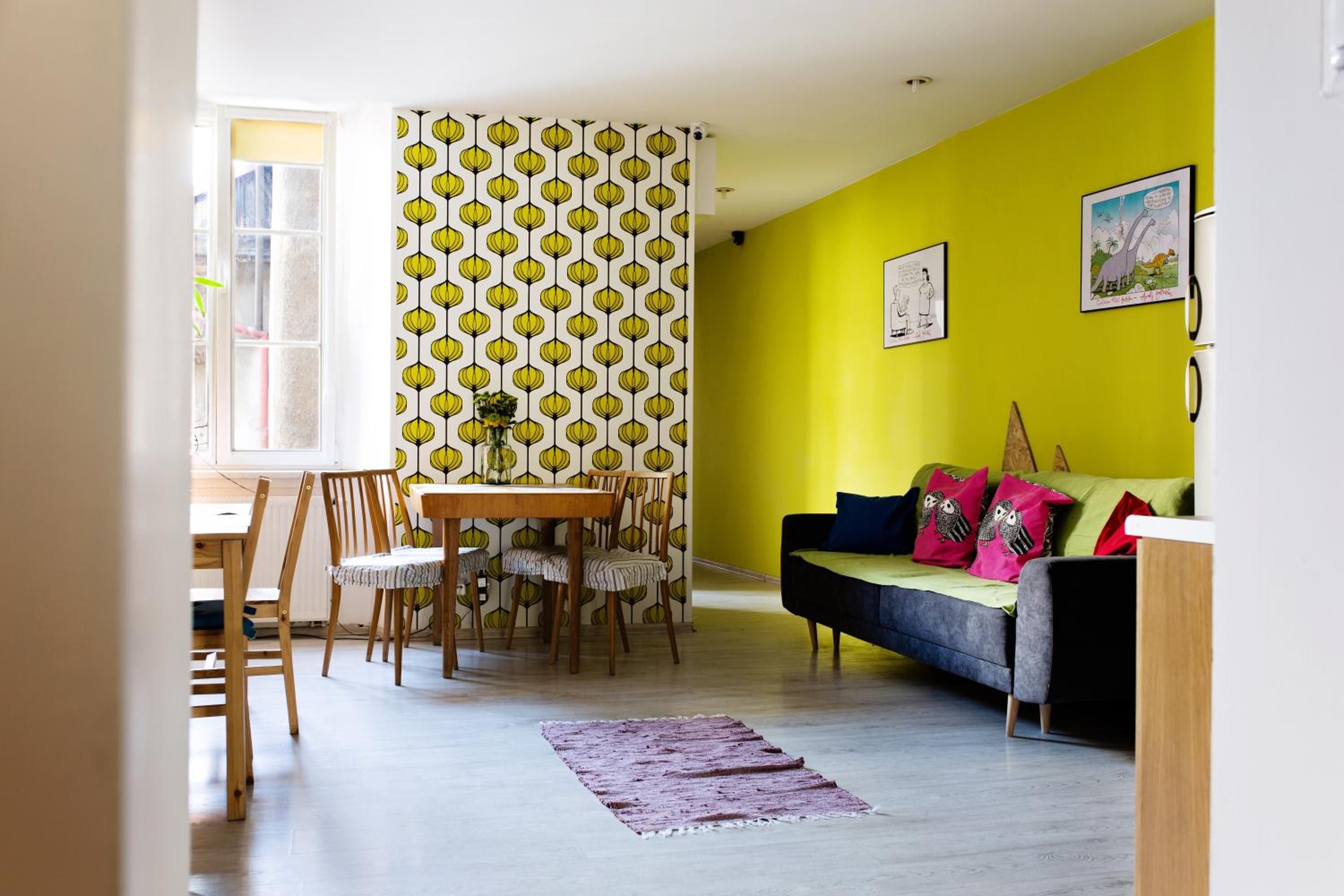 Quarto com uma mesa de jantar e cadeiras, um sofá com almofadas e um papel de parede estampado.