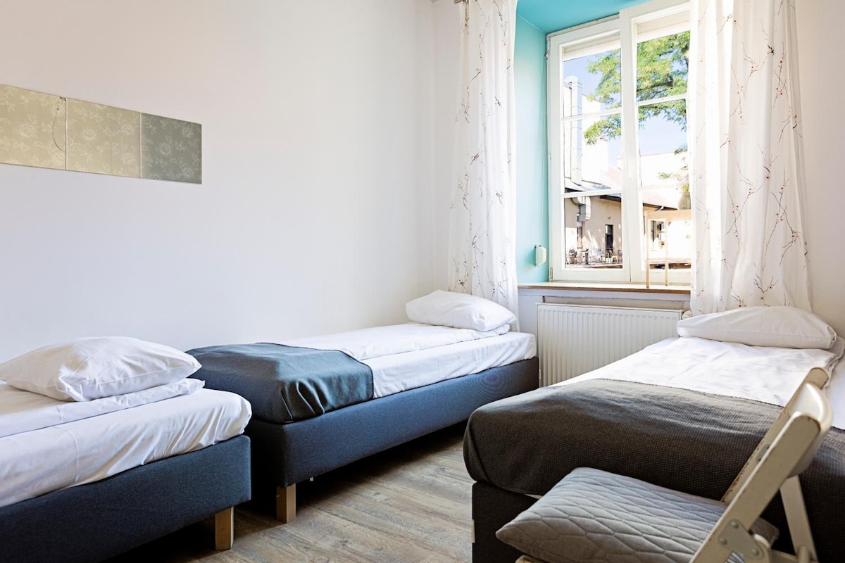 A room with two single beds, a window with curtains, and a radiator.
