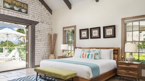 A bedroom with a bed, bedside tables, a bench, a window, and a view of the outdoors. - Callaloo Cottage (Providenciales)