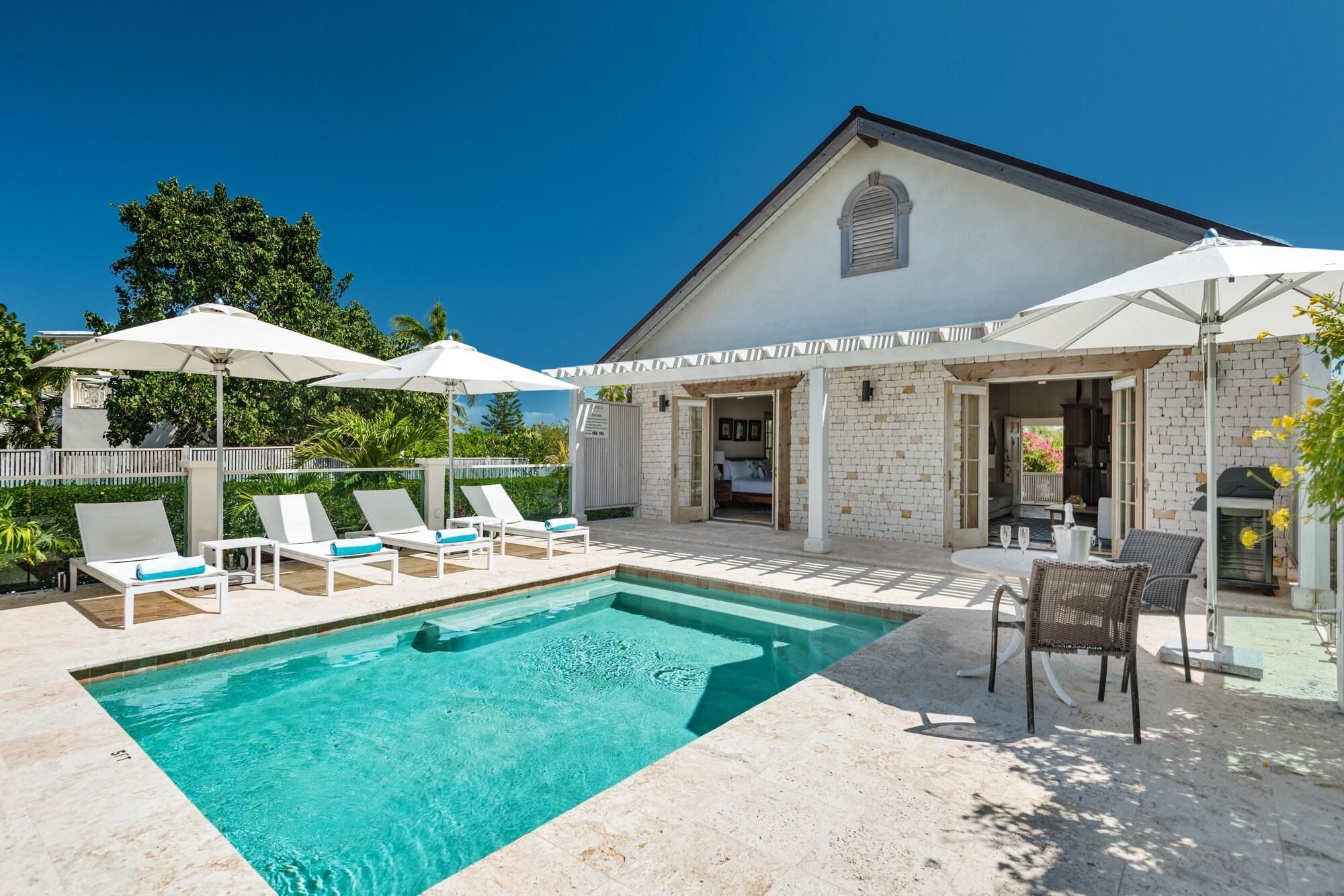 A poolside area with lounge chairs, umbrellas, and a clear blue pool.