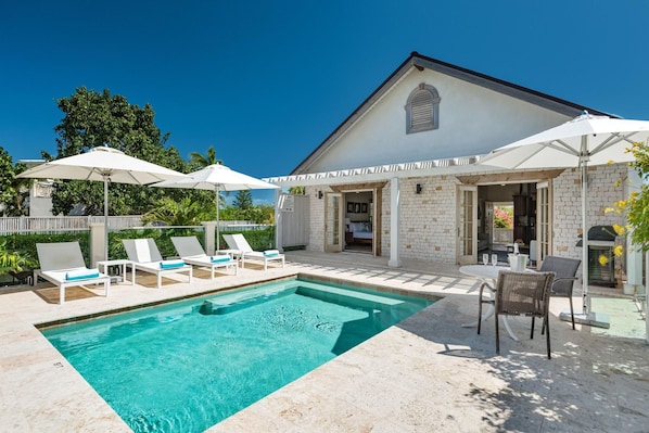 Un espace aménagé au bord de la piscine, avec des chaises longues, des parasols et une piscine à l’eau d’un bleu limpide.
