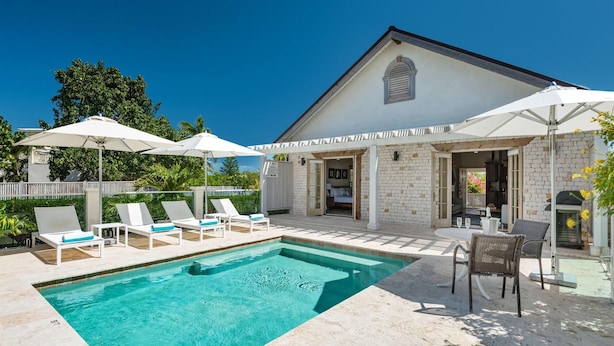A poolside area with lounge chairs, umbrellas, and a clear blue pool. - Callaloo Cottage (Providenciales)