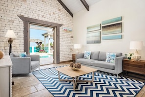Un salon avec un canapé gris, une table basse et un tapis à motifs. On y trouve un mur en briques et une vue sur un espace extérieur.