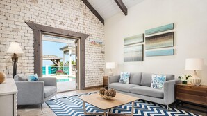 A living room with a grey sofa, a coffee table, and a patterned rug. There is a brick wall and a view of an outdoor area. - Callaloo Cottage (Providenciales)