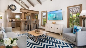 A spacious living area with a kitchen, a dining area with wicker chairs, a flat-screen TV, and a sofa with decorative pillows. - Callaloo Cottage (Providenciales)