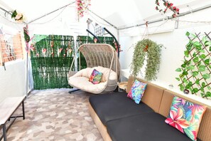 A cozy outdoor seating area with a hanging chair, a cushioned bench, and a wall-mounted plant. - Heated Jacuzzi & Luxury Garden Retreat Larnaca (Larnaka)