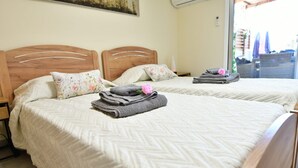 Une chambre d’hôtel avec deux lits, chacun doté d’une tête de lit en bois, de draps blancs et d’un coussin à motifs floraux. On trouve des serviettes et une fleur rose sur l’un des lits.