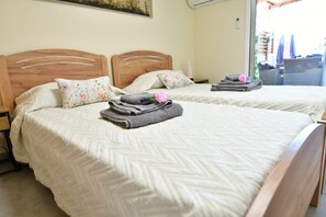 Habitació d'hotel amb dos llits, cadascun amb capçalera de fusta, roba de llit blanca i un coixí amb flors. Hi ha tovalloles i una flor rosa a un dels llits.