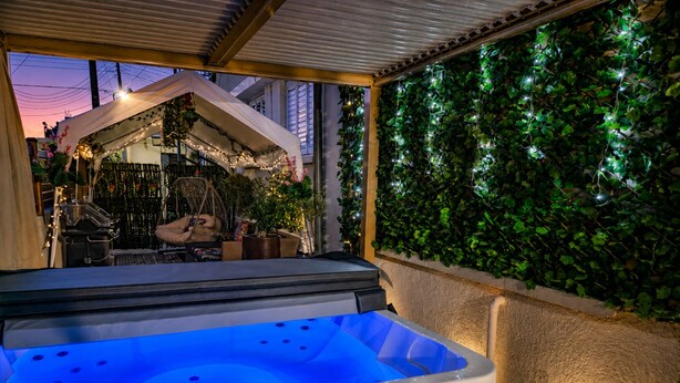 Un bain à remous doté d’un panneau de commande numérique, entouré d’une terrasse couverte agrémentée d’un mur de verdure et de guirlandes lumineuses.