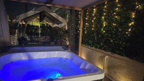 Un bain à remous doté d’un écran numérique, entouré d’une terrasse couverte agrémentée de guirlandes lumineuses et d’un mur de verdure.