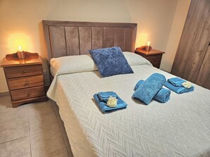A neatly made bed with a white quilt and blue pillows, two bedside tables with lamps, and a wooden headboard. - Heated Jacuzzi & Luxury Garden Retreat Larnaca (Larnaka)