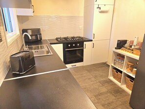 A compact kitchen with a toaster, sink, stove, oven, and a shelf with kitchenware. - Heated Jacuzzi & Luxury Garden Retreat Larnaca (Larnaka)