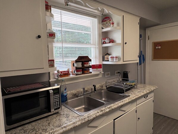 A kitchen with a microwave, sink, and various food items on shelves.