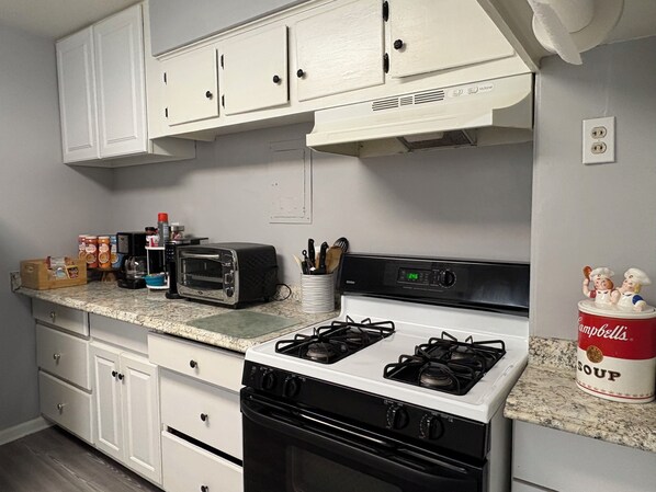 A kitchen with white cabinets, a gas stove, a toaster, and a can of soup on the counter.