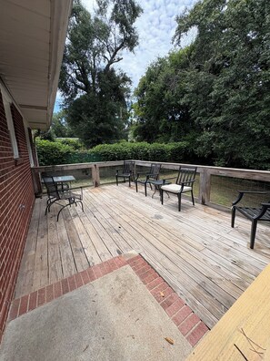 A wooden deck with outdoor furniture, a brick wall, and a view of trees and greenery.