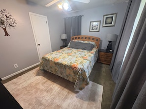 A bedroom with a bed, a nightstand, a lamp, a wall-mounted tree decoration, and a door.