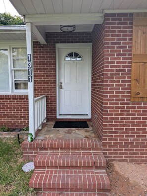 A brick house with a white front door, a small porch, and a mailbox.