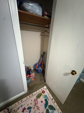 A narrow hallway with a door on the right, a shoe rack on the left, and a colorful rug on the floor.