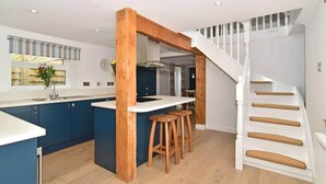 A modern kitchen with a central island, wooden stools, and a staircase with white railings. - 2bed Cottage Johnshaven - Family Friendy (Montrose)