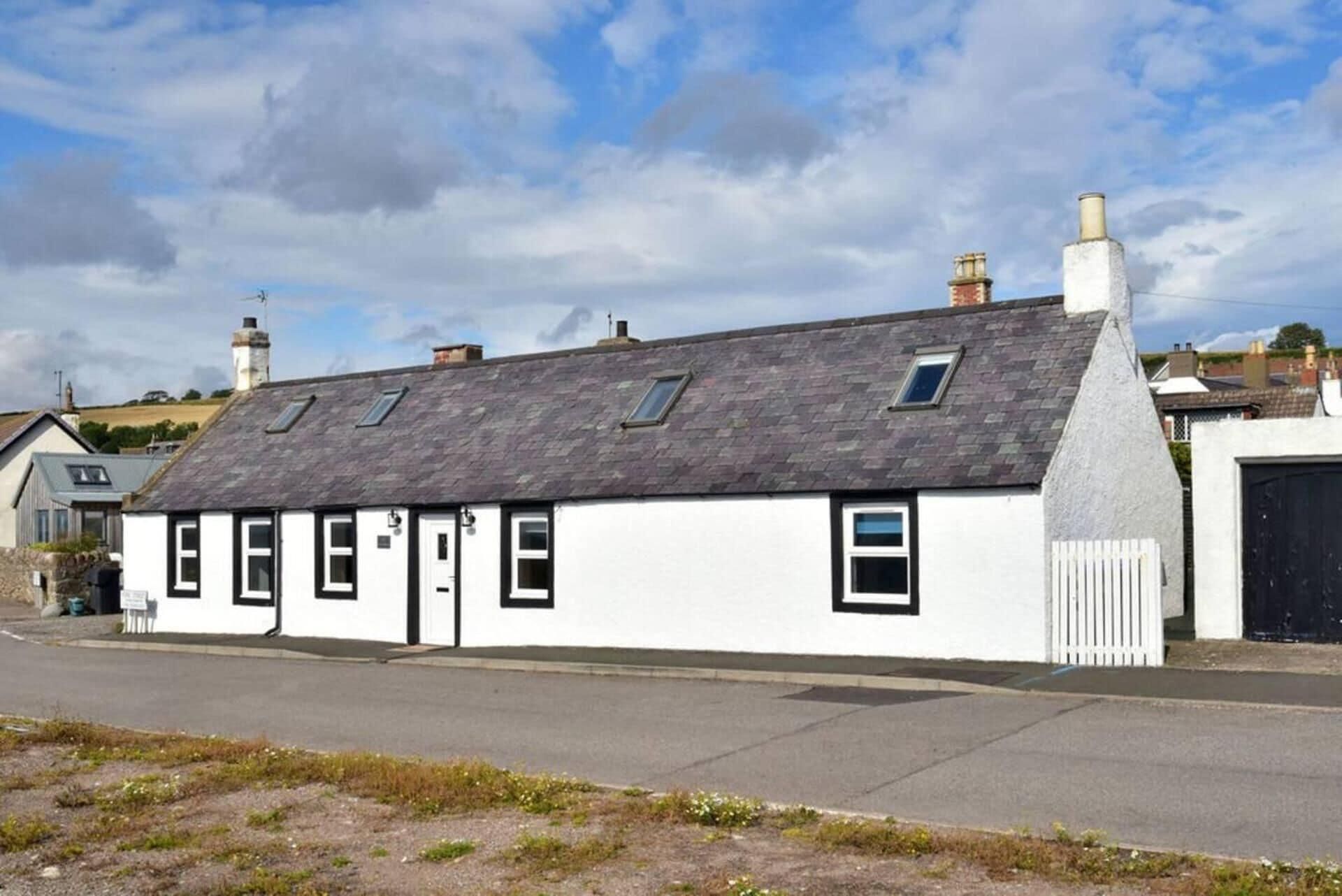 A white building with a grey roof and multiple windows, located on a street with a clear sky.