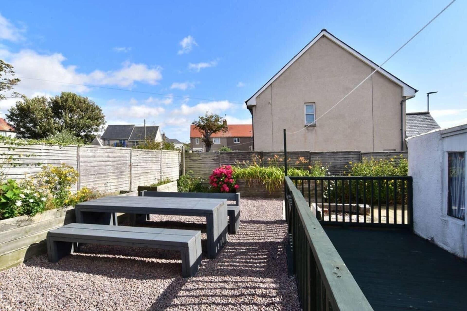 A backyard with a patio area, a wooden fence, and a building in the background.