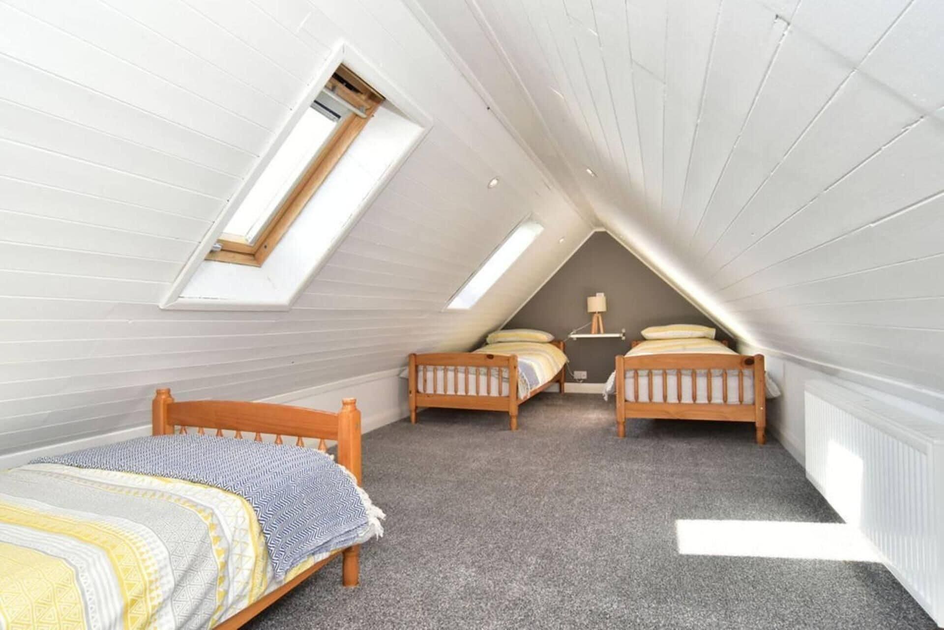 A small attic bedroom with two wooden beds, a skylight, and a radiator.