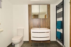 Ein Badezimmer mit Toilette, einem Waschbecken mit Spiegel darüber und einem Handtuchhalter mit Handtüchern.