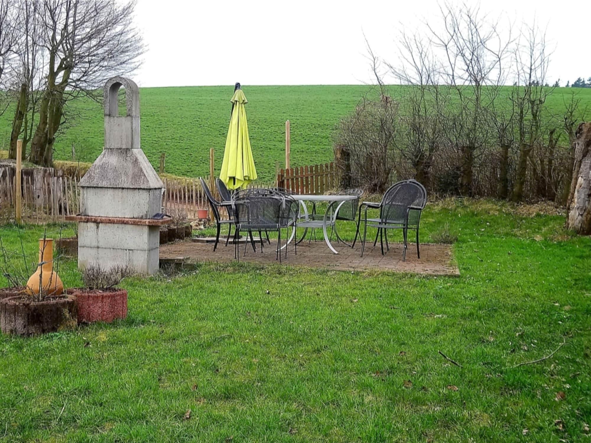 An outdoor patio with a table and chairs, a yellow umbrella, and a concrete structure.