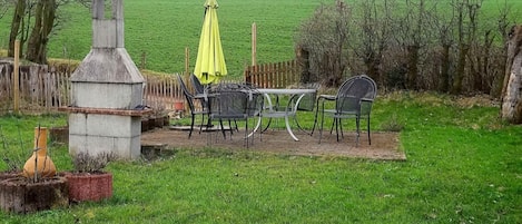 An outdoor patio with a table and chairs, a yellow umbrella, and a concrete structure.