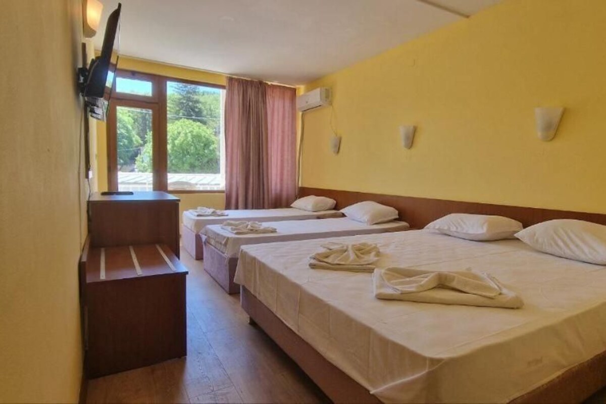 A hotel room with three beds, a bench, and a window with curtains.