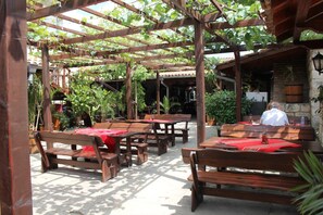 An outdoor patio with wooden tables and benches, covered by a wooden pergola with vines. - Complex Dobrudja (Balchik)