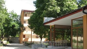 A building with a covered outdoor area, a staircase, and a tree in front.