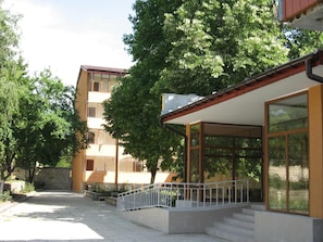 A building with a covered outdoor area, a staircase, and a tree in front. - Complex Dobrudja (Balchik)