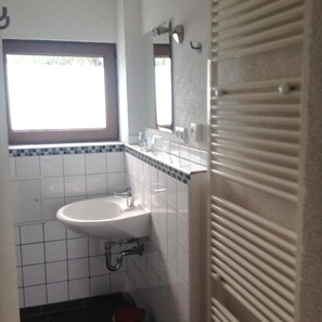 Een badkamer met een wit wastafelmeubel, een spiegel erboven en een raam boven het wastafelmeubel.
