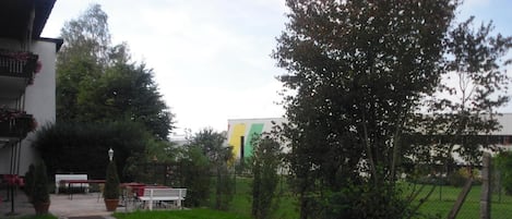 A gravel pathway leading to a seating area with benches and a table, surrounded by greenery and a fence.