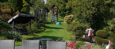 Un jardin avec un espace de jeux, un coin salon abrité et un étang.