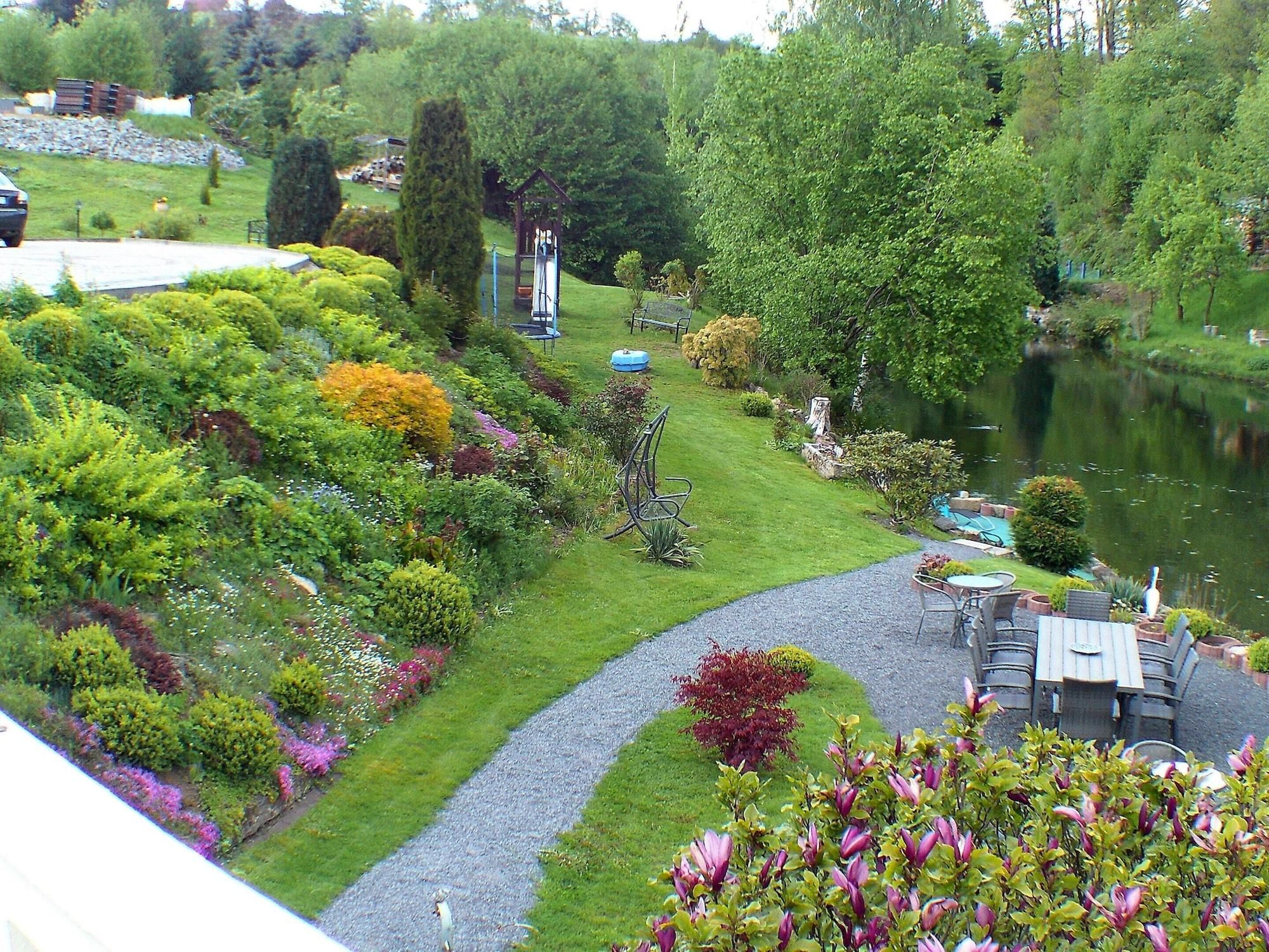 Een tuin met een vijver, een prieel en een zithoek met tafels en stoelen.