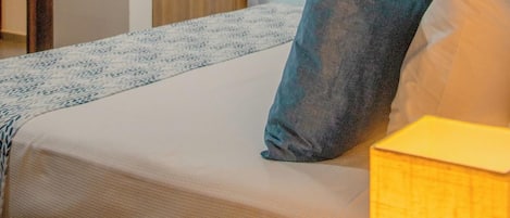 Habitación de hotel con cama, mesita de noche, armario de madera y ventana con cortinas translúcidas.