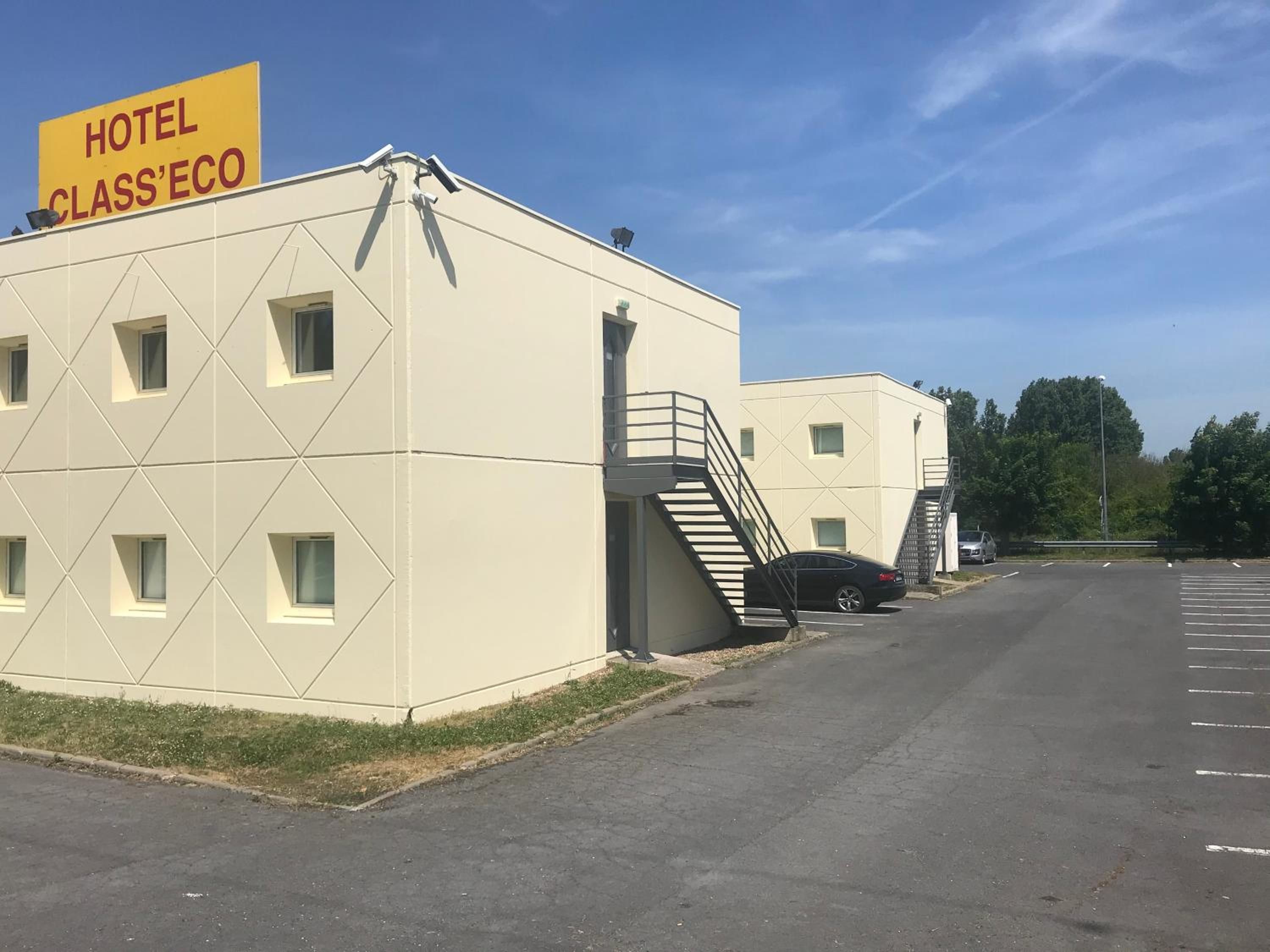 A building with a sign reading 'HOTEL CLASS'ECO' and a parking lot with a car.