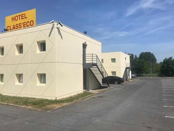 A building with a sign reading 'HOTEL CLASS'ECO' and a parking lot with a car.