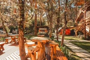 An outdoor area with wooden tables and benches, surrounded by trees and a small building. - La Brume Pousada (Campos do Jordão)