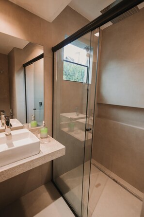 A modern bathroom with a glass shower enclosure, a large mirror, and a countertop with two sinks and toiletries. - La Brume Pousada (Campos do Jordão)